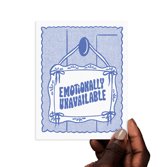 Hand holding card that says 'Emotionally unavailable' in blue hand lettering on a hanging sign design.