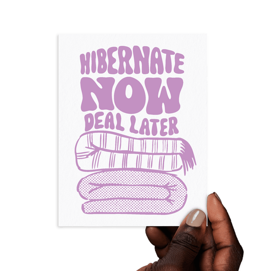 Hand holding card with 'Hibernate now, deal later' in lavender hand lettering with cozy blanket illustration.