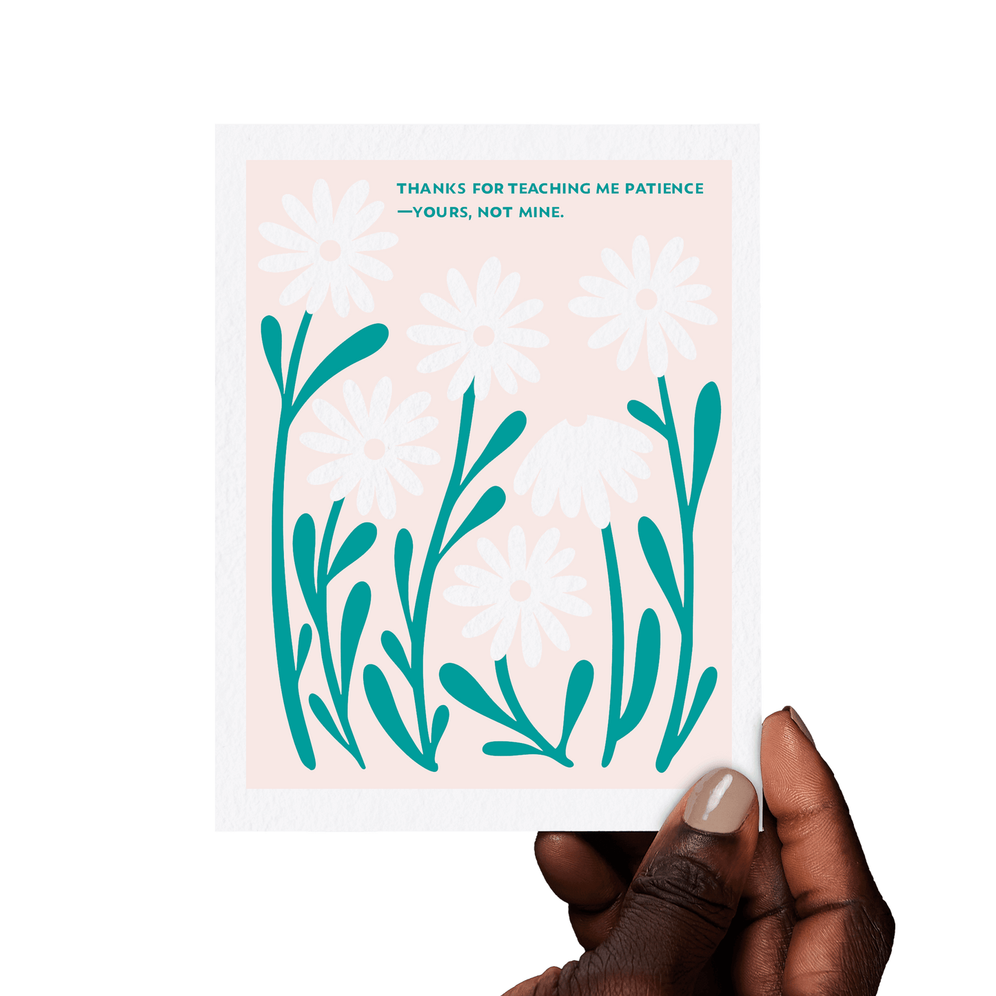 Hand holding a floral greeting card with ‘Thanks for teaching me patience—yours, not mine.’ in teal hand lettering, framed by white daisies on a pink background.