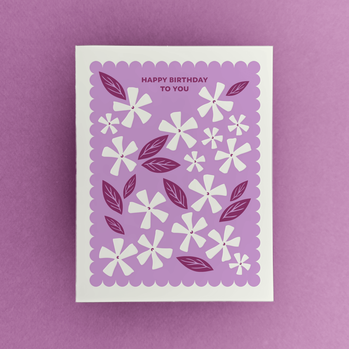 Letterpress birthday card with white floral illustrations, berry-toned leaves, and a purple scalloped border reading “Happy Birthday to You.