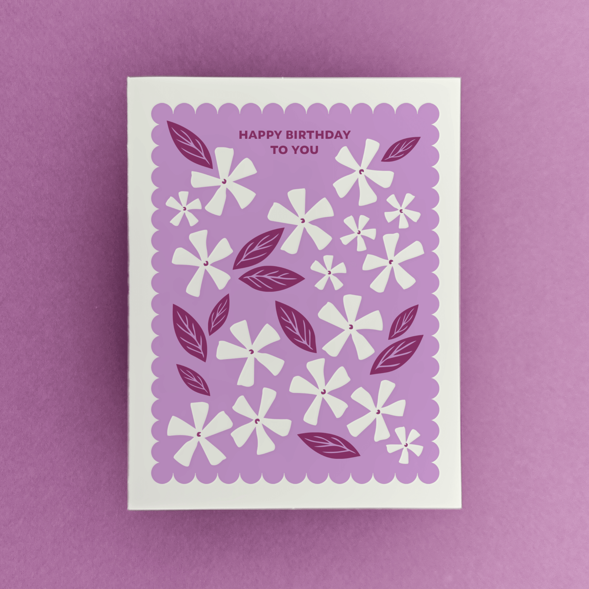Letterpress birthday card with white floral illustrations, berry-toned leaves, and a purple scalloped border reading “Happy Birthday to You.