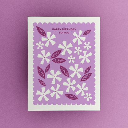 Letterpress birthday card with white floral illustrations, berry-toned leaves, and a purple scalloped border reading “Happy Birthday to You.