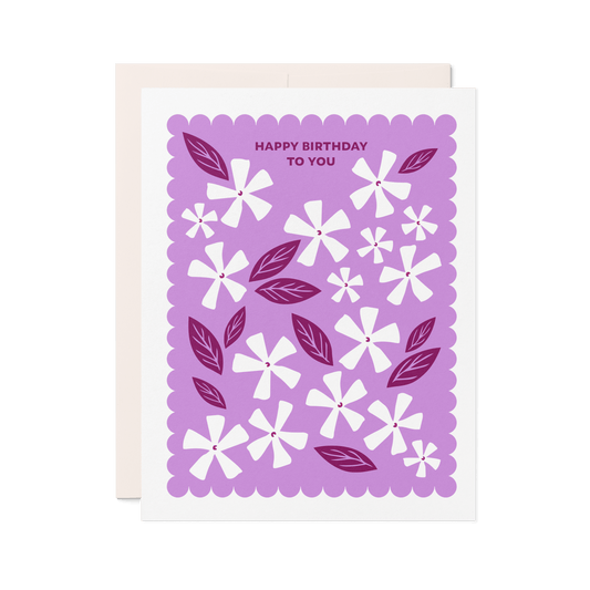 Letterpress birthday card with white floral illustrations, berry-toned leaves, and a purple scalloped border reading “Happy Birthday to You.