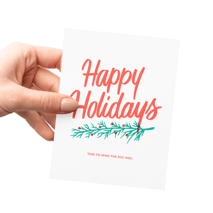 Hand holding a card with 'Happy Holidays' text and a evergreen branch design.