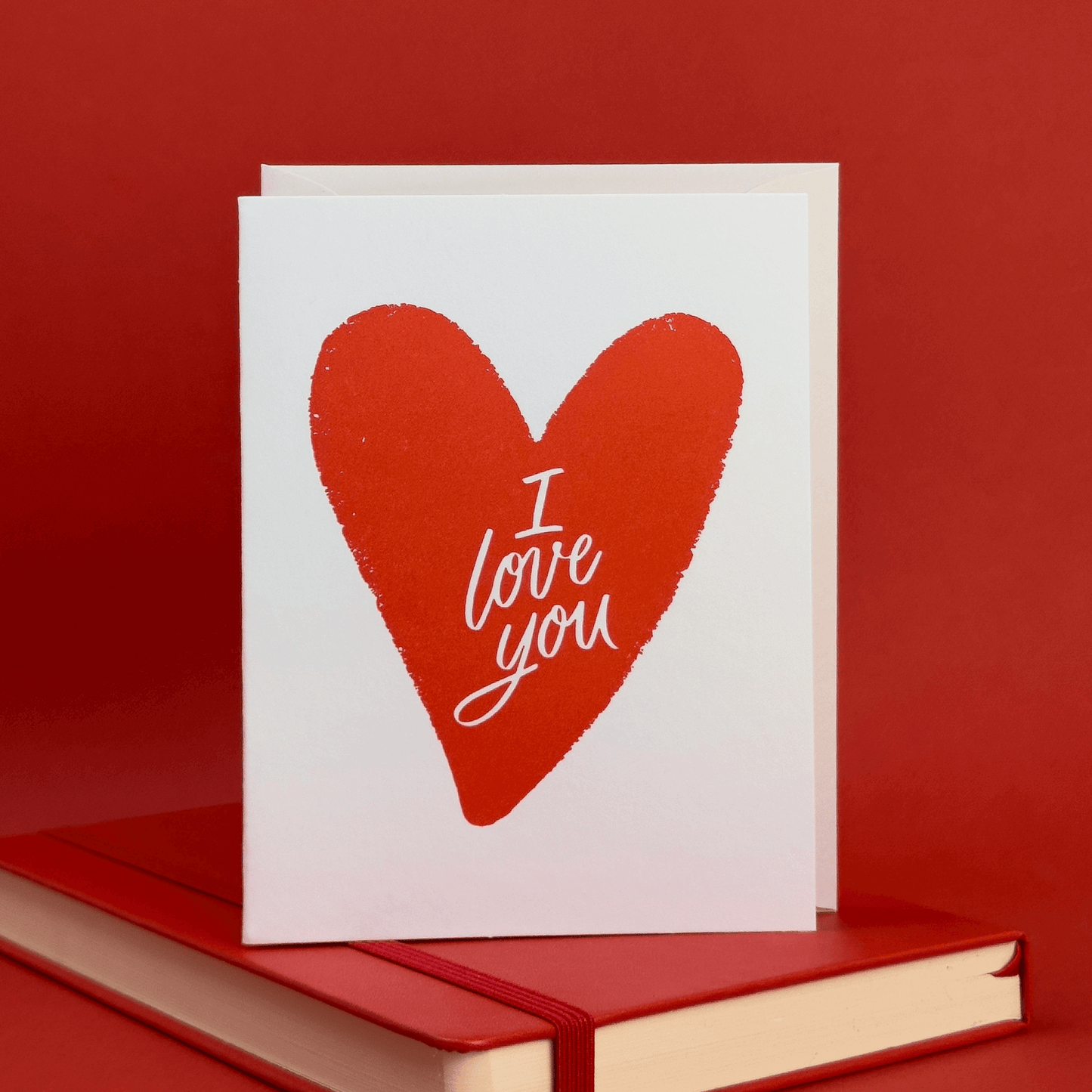 Card with a red heart illustration with 'I love you' hand lettered inside of it on a red background.