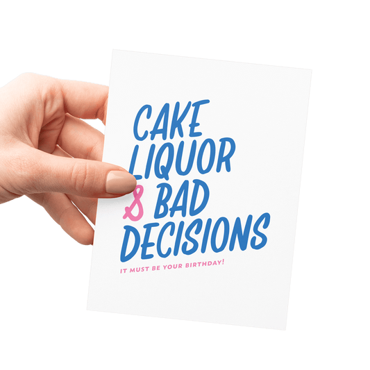 Hand holding a humorous birthday card with 'Cake, Liquor & Bad Decisions' in blue and pink hand lettering.