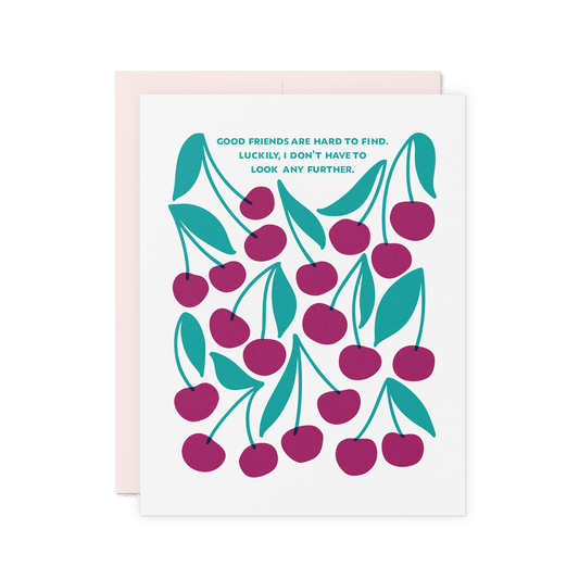 Friendship card with ‘Good friends are hard to find. Luckily, I don’t have to look any further.’ in teal hand lettering, featuring an illustrated pattern of merlot-colored cherries and green leaves on thick cotton paper.