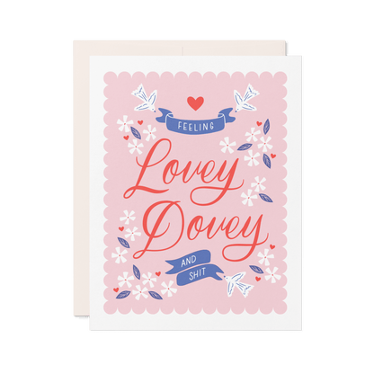 Love card with pink background that reads 'Feeling Lovey Dovey and Shit' in red and blue lettering with floral and bird illustrations.