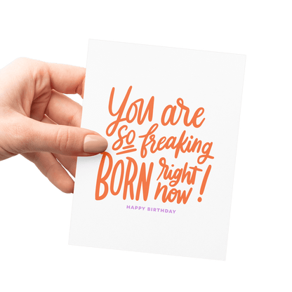 Hand holding a funny birthday card with 'You are so freaking born right now!' in orange hand lettering, letterpress printed on thick cotton paper.