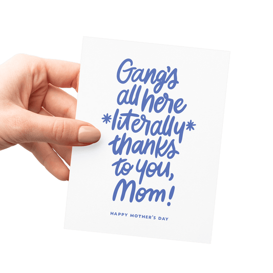 Hand holding a humorous Mother’s Day card with ‘Gang’s all here literally thanks to you, Mom!’ in blue hand lettering.