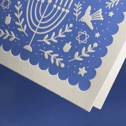 Close-up detail of letterpress card with white cut-out designs on a blue background.