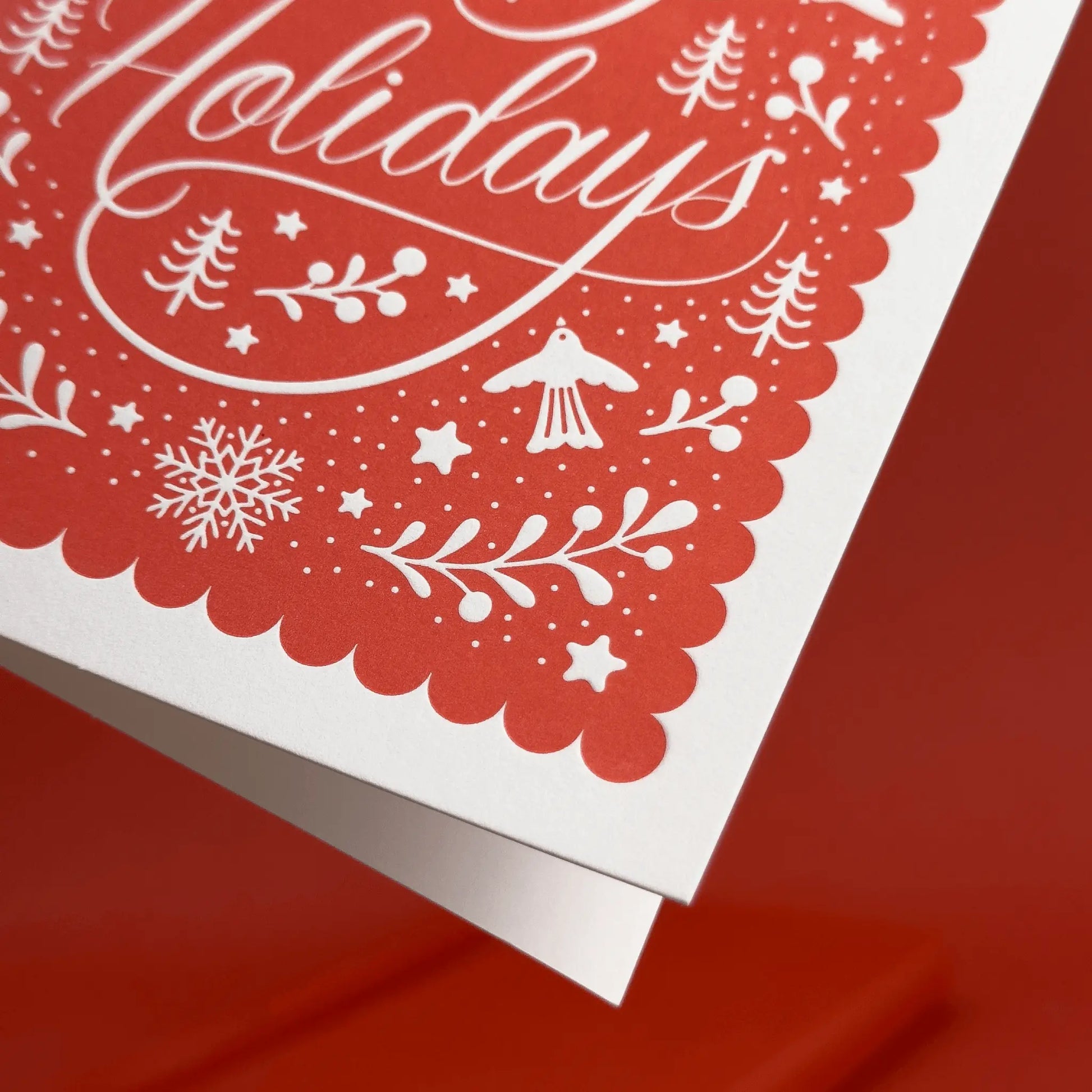 Closeup of red letterpress holiday card with white festive illustrations and elegant script.