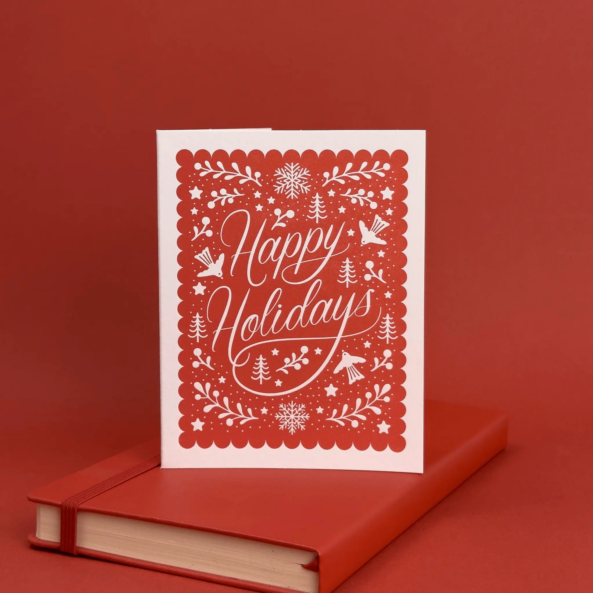Red holiday card with white script reading 'Happy Holidays' displayed on a red book and background.