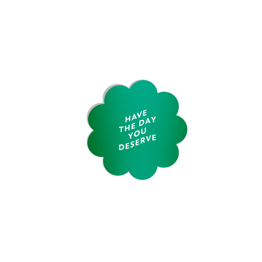 Funny green flower-shaped sticker with ‘Have the Day You Deserve’ in white lettering, featuring a silky matte mirror finish.