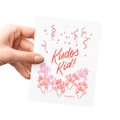 Hand holding an encouragement card with cheering hands, confetti, and celebratory lettering, letterpress printed.