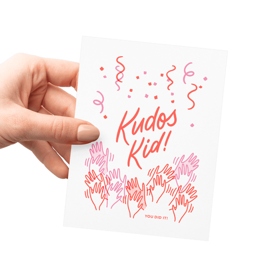 Hand holding an encouragement card with cheering hands, confetti, and celebratory lettering, letterpress printed.