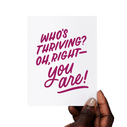 Hand holding a congratulations card with ‘Who’s thriving? Oh, right—you are!’ in burgundy hand lettering on white cotton paper.