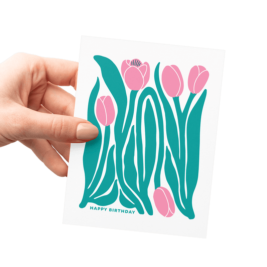 Hand holding tulip illustration birthday card, showing pink tulips and green leaves, letterpress printed.