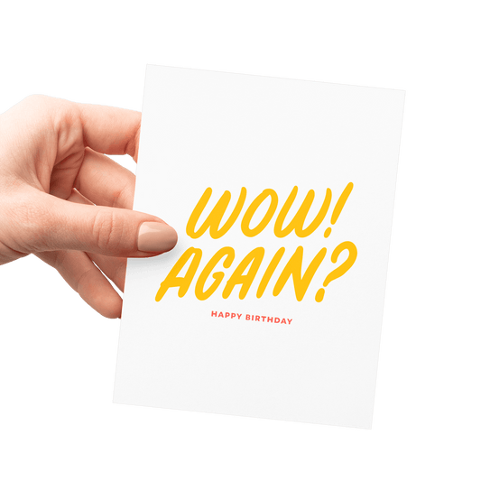 Hand holding a humorous birthday card with 'Wow! Again?' in yellow hand lettering.